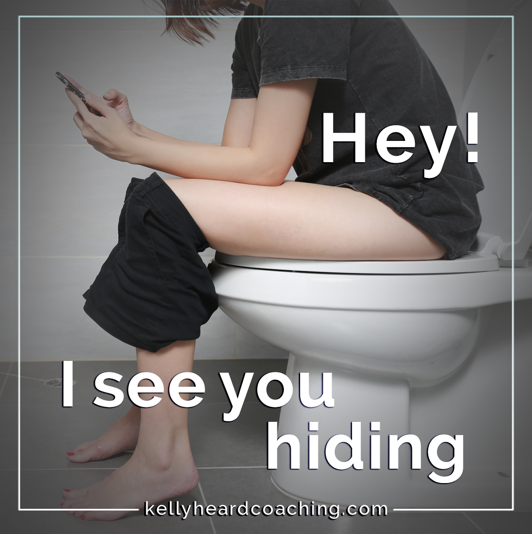 woman in a bathroom using her phone stop hiding Kelly Heard Coaching